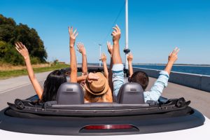Just fun and road ahead. Rear view of young happy people enjoying road trip in their convertible and raising their arms up